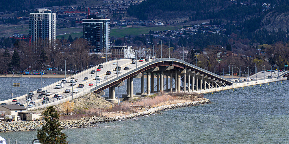 Picture of Kelowna bridge from the west shore with high-rise buildings and mountains in the background